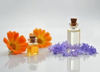 Na zdjęciu dwie buteleczki zawierajace olejki kosmetyczne, w otoczeniu kwatów
