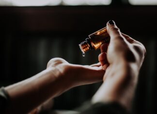 Olejowanie włosów poprawia ich kondycję. Na zdjęciu kobieta trzyma buteleczkę olejki, kropla opada jej na dłoń. Jest to poprawna metoda aplikacji olejku.
