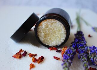 Jak zrobić peeling ust prawidłowo? To nie łatwa sztuka. Na zdjęciu słoiczek z domowej roboty peelingiem naturalnym na cukrze. Obok lawenda i płatki kwiatów.
