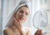 Olejowanie włosów to prosta metoda regeneracji włosów. Na zdjęciu kobieta przegląda się w lusterku, włosy ma owinięte ręcznikiem.