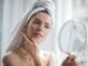 Olejowanie włosów to prosta metoda regeneracji włosów. Na zdjęciu kobieta przegląda się w lusterku, włosy ma owinięte ręcznikiem.