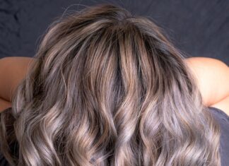 Różne rodzeje włosów potrzebują różnej pielęgnacji. Na zjęciu kobieta prezentuje swoje długie, kręcone farbowane na szaro włosy.